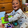 toddler, child, toy, pajamas, smile, happy, indoor, carpet, wooden_furniture, play, colorful, shape_sorter, baby, cute, hands, face, sitting, cozy, room, fun
