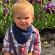 Ivan is registered to the contest to win money with this photo: toddler, child, outdoor, flower, purple_flower, plant, nature, greenery, face, portrait, plaid_shirt, suspenders, bib, blue_eyes, blond_hair, sunlight, garden, dirt, clothing, expression