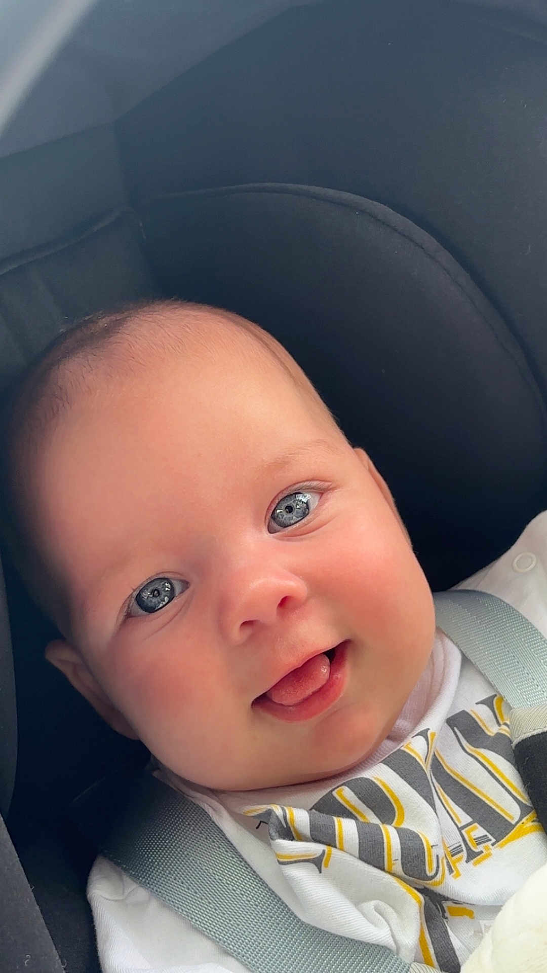 Capucine participe au concours pour gagner de l'argent avec cette photo : baby, infant, face, blue_eyes, smile, tongue_out, car_seat, seatbelt, white_clothing, close_up, child, cute, happy, skin, head, person, portrait, young, seat, babywearing