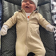 Ezra is registered to the contest to win money with this photo: baby, infant, child, onesie, hat, mittens, smile, happy, lying_down, cushion, patterned, black_and_white, cozy, indoor, soft_light, cute, warm_clothing, face, person, portrait