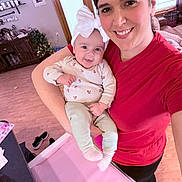 Everly is registered to the contest to win money with this photo: woman, baby, smile, indoor, living_room, headband, red_shirt, wooden_floor, christmas_tree, furniture, window, door, decor, person, family, happy, holding, portrait, clothing, home