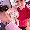 woman, baby, smile, indoor, living_room, headband, red_shirt, wooden_floor, christmas_tree, furniture, window, door, decor, person, family, happy, holding, portrait, clothing, home