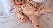 Everly is registered to the contest to win money with this photo: baby, child, infant, pajamas, strawberry_pattern, bed, white_bedspread, pillow, smile, cute, lying_down, happy, indoors, person, sleepwear, soft, comfortable, cozy, young, relaxed