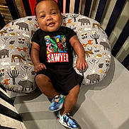 Sawyer is registered to the contest to win money with this photo: baby, infant, crib, pillow, superhero, clothing, shoes, pattern, smiling, cute, child, indoor, person, apparel, footwear, happy, resting, colorful, marvel, decor