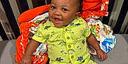 Sawyer joined the competition — help win amazing prizes! baby, child, smiling, dinosaur_print, shorts, shirt, blanket, orange_blanket, footwear, sandals, happy, indoor, crib, person, cute, seated, infant, clothing, bright_colors, portrait