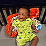 baby, child, smiling, dinosaur_print, shorts, shirt, blanket, orange_blanket, footwear, sandals, happy, indoor, crib, person, cute, seated, infant, clothing, bright_colors, portrait