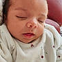 baby, sleeping, infant, onesie, white_clothing, patterned_clothing, animal_print, berry_print, face, head, closed_eyes, soft_texture, red_leather, couch, indoors, cozy, resting, peaceful, newborn, portrait