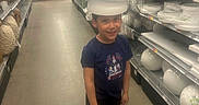 Nathan is registered to the contest to win money with this photo: child, boy, store, aisle, shelves, styrofoam, helmet, shopping, casual_clothing, blue_shoes, black_pants, smiling, indoor, floor, boxes, person, retail, home_goods, fun, headwear