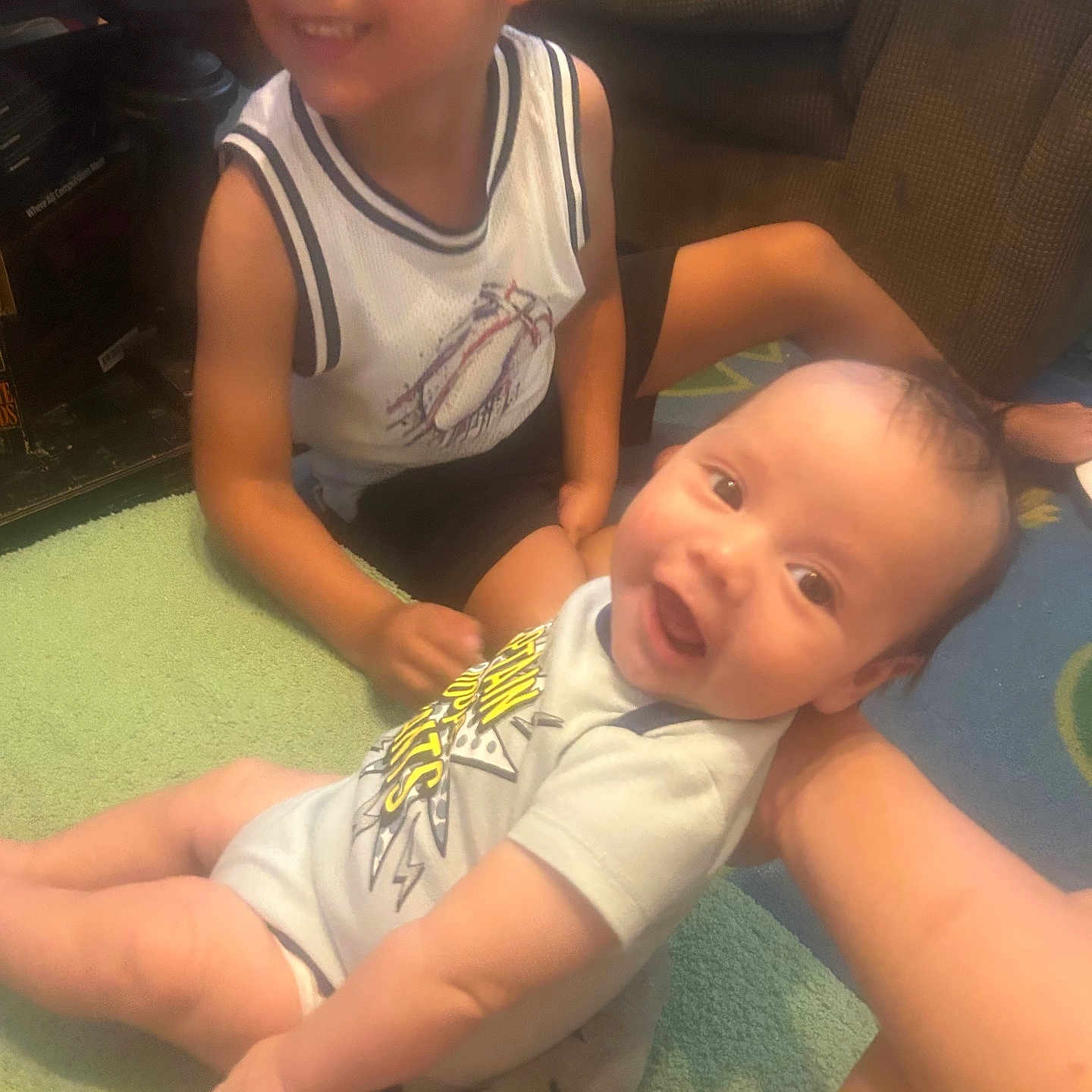 Justin is registered to the contest to win money with this photo: baby, child, smiling, indoor, living_room, couch, carpet, sitting, happy, person, toddler, clothing, shorts, onesie, arm, face, hair, toy, furniture, playtime