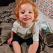 Legend joined the competition — help win amazing prizes! child, red_hair, curly_hair, smile, bed, pillow, blanket, tshirt, shorts, indoor, happy, cute, young_child, person, face, sitting, wipes, room, casual, curly