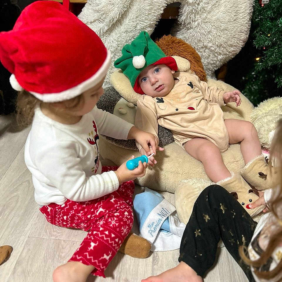 Rita a rejoint le concours — aidez-le/la à gagner de superbes lots ! baby, boots, child, christmas, cozy, cute, elf_hat, family, festive, floor, fun, happy, holiday, indoor, pajamas, playing, plush_chair, santa_hat, toddler, toy