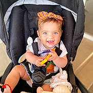 Rita participe au concours pour gagner de l'argent avec cette photo : baby, child, stroller, headband, toy, doll, blanket, smiling, happy, blue_eyes, clothing, sitting, indoor, infant, cute, playful, person, seatbelt, footwear, toddler