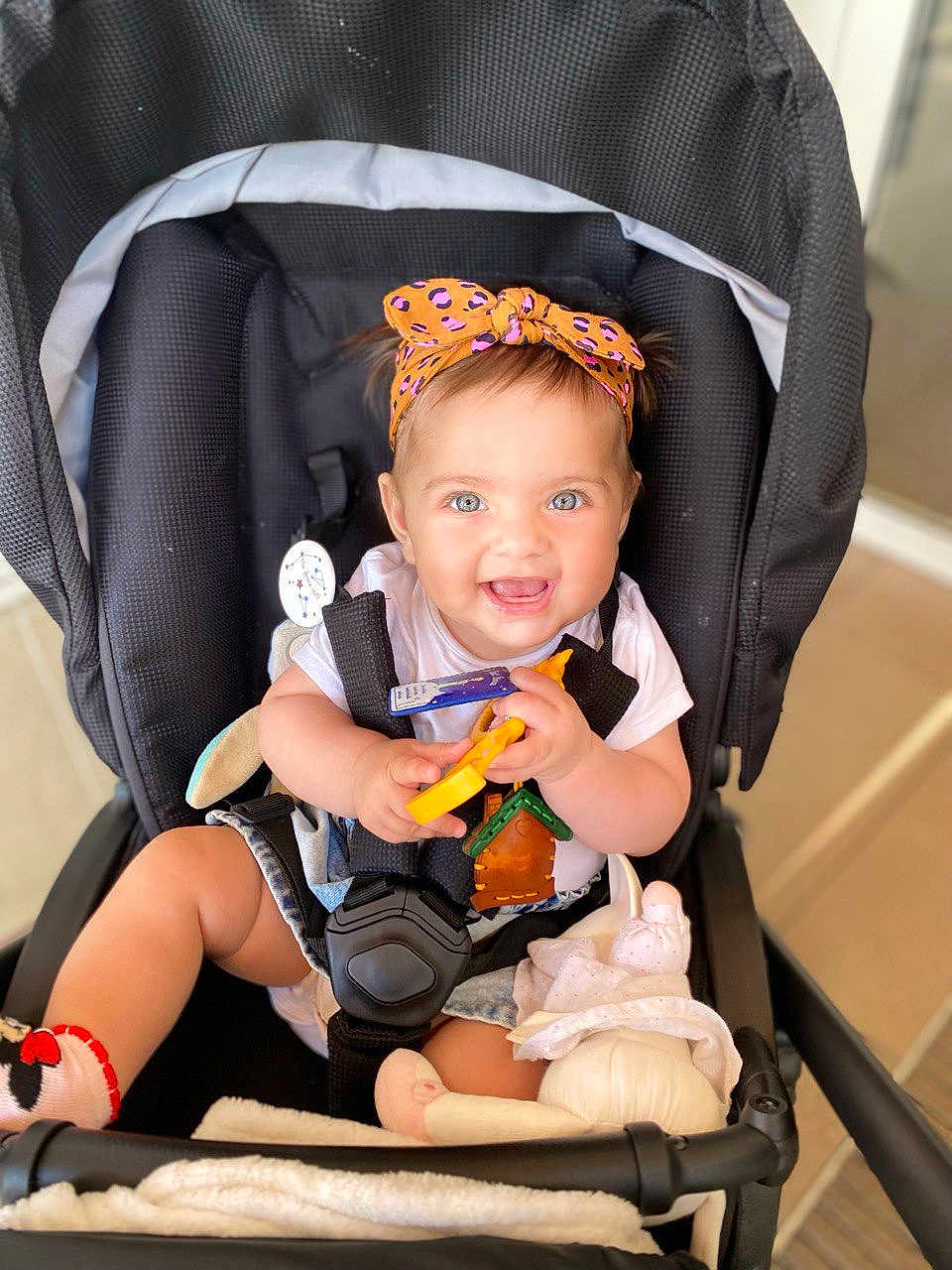 Rita participe au concours pour gagner de l'argent avec cette photo : baby, child, stroller, headband, toy, doll, blanket, smiling, happy, blue_eyes, clothing, sitting, indoor, infant, cute, playful, person, seatbelt, footwear, toddler