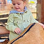 animal, animal_stripe, casual_clothing, child, curious, daylight, gentle, hair_clips, hand, interaction, jacket, nature, outdoor, person, petting, smiling, soft_focus, support, toddler, young_child