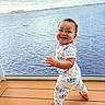 Laviarus is registered to the contest to win money with this photo: apparel, baby, child, cloudy, cute, daylight, deck, dinosaur_pajamas, footwear, happy, ocean, outdoor, person, playful, sky, smiling, standing, toddler, water, window