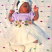 Neriah is registered to the contest to win money with this photo: baby, sleeping, infant, headband, tutu, floral, knitted_blanket, purple_top, white_skirt, socks, cozy, cute, peaceful, portrait, child, laying_down, soft_lighting, indoor, clothing, adorable