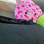 black_cat, cat, sleeping, plush_pillow, pink_pillow, green_pillow, couch, indoor, window, natural_light, relaxing, cozy, furniture, pet, animal, resting, soft_texture, stuffed_toy, home, cute