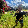 child, toddler, outdoor, backyard, grass, smiling, portrait, sunlight, clouds, sky, flowers, roses, sunflowers, beaded_hair, braids, colorful_clothing, sandals, toys, atv, house