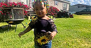 Jaleriah is registered to the contest to win money with this photo: child, toddler, outdoor, lawn, grass, house, mobile_home, sunlight, blue_sky, clouds, flowers, flower_bush, grill, barbecue, atv, vehicle, car, beaded_hair, colorful_clothing, portrait