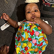 Gianna joined the competition — help win amazing prizes! baby, infant, child, portrait, smiling, curious, flower_headband, colorful_clothing, fruit_pattern, dress, couch, indoor, sitting, lying_down, hand_to_mouth, dark_skin, fashion, closeup, family, photography