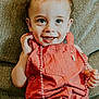 Beckham is registered to the contest to win money with this photo: toddler, child, smiling, overalls, orange_clothing, bead_necklace, sitting, couch, happy, face, hands, indoor, portrait, cute, young_child, clothing, person, baby, expression, furniture