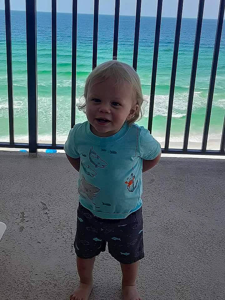 Braxton is registered to the contest to win money with this photo: baby, baby_toddler_clothing, barefoot, bermuda_shorts, blue, child, fence, happy, human_body, human_leg, line, person, shorts, sky, sleeve, smile, standing, summer, t_shirt, toddler