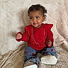 toddler, child, red_clothing, jeans, chain, curly_hair, sitting, blanket, indoor, footwear, cute, smiling, portrait, baby, fashion, happy, comfortable, casual, young_child, playful