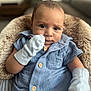 baby, infant, blue_clothing, mittens, cute, portrait, face, child, sitting, furry_cushion, closeup, indoors, cozy, soft_light, young_child, expression, buttoned_shirt, small_hands, comfortable, adorable