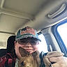 Baby Bear is registered to the contest to win money with this photo: person, dog, car_interior, hat, cap, glasses, smile, pet, brown_dog, casual_clothing, seat, window, hand, closeup, indoor, companion, resting_dog, human_animal_interaction, portrait, happy