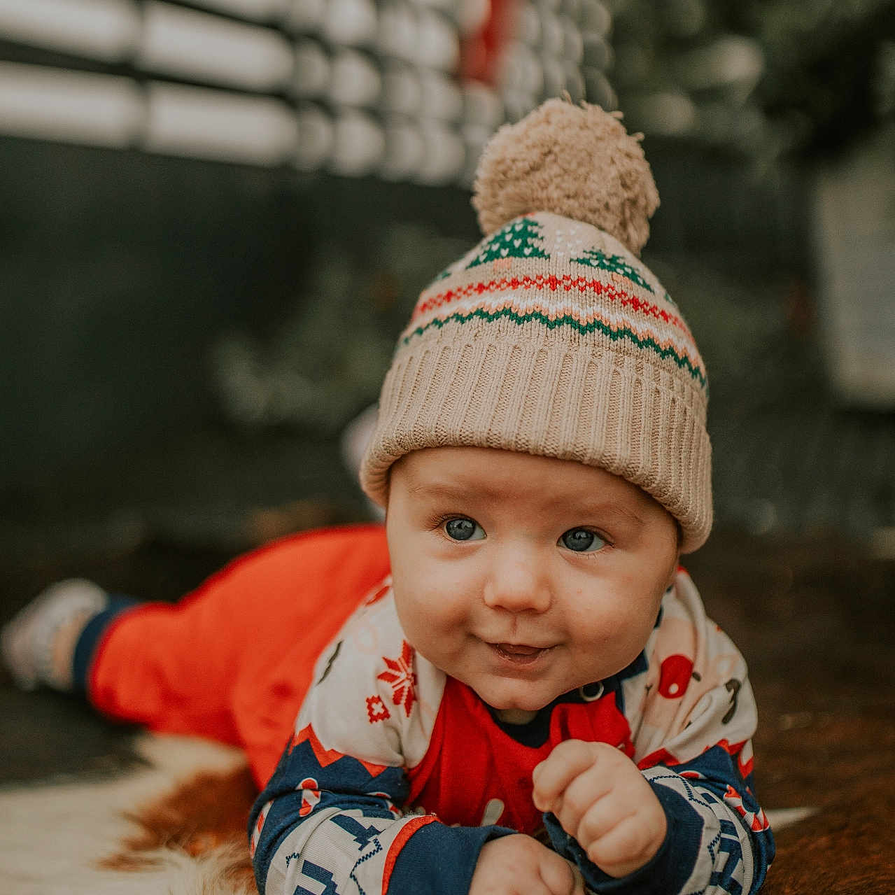 Corbyn is registered to the contest to win money with this photo: baby, blue_eyes, child, close_up, cozy, cute, face, fur_rug, happy, hat, indoors, infant, lying_down, patterned_sleeves, pom_pom, portrait, red_clothing, smiling, warm, winter_clothing