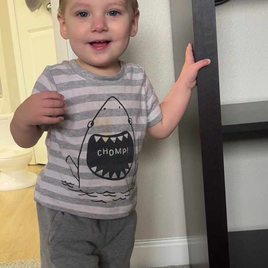 Zaiyon is registered to the contest to win money with this photo: barefoot, carpet, casual_clothing, child, door, floor, furniture, happy, home, indoor, person, portrait, shelf, shirt, shorts, smile, standing, toddler, towel, wall