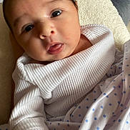 Adira joined the competition — help win amazing prizes! baby, infant, close_up, face, tongue_out, white_clothing, blanket, blue_polka_dots, hand, soft_lighting, indoors, cute, newborn, person, skin, expression, head, eyes, wrinkled_clothing, cozy
