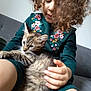 child, kitten, cat, curly_hair, green_dress, floral_embroidery, couch, indoor, hand, pet, cute, young, furry, lap, domestic_animal, comfort, closeup, portrait, relaxed, cozy