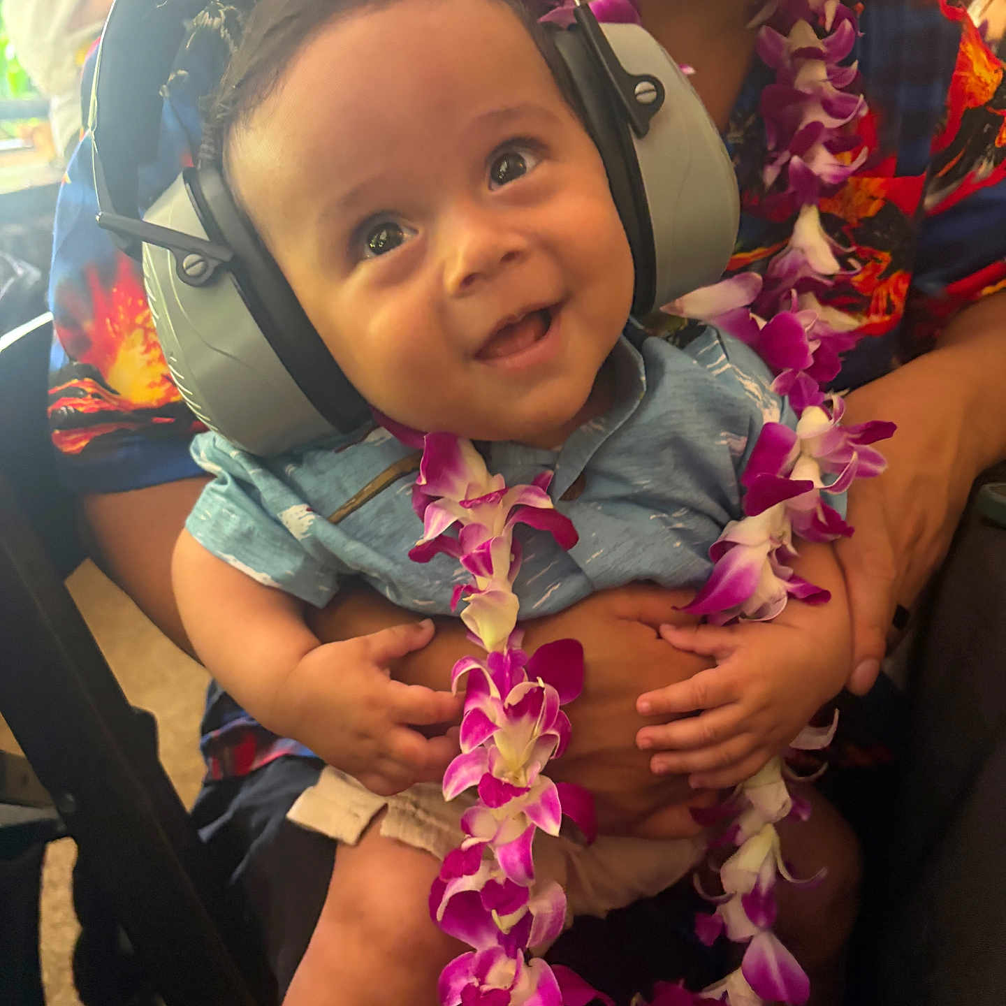 Silas is registered to the contest to win money with this photo: baby, child, headphones, lei, flower_garland, happy, smiling, person, adult, hand, clothing, colorful, portrait, indoor, celebration, cute, toddler, holding, festival, family