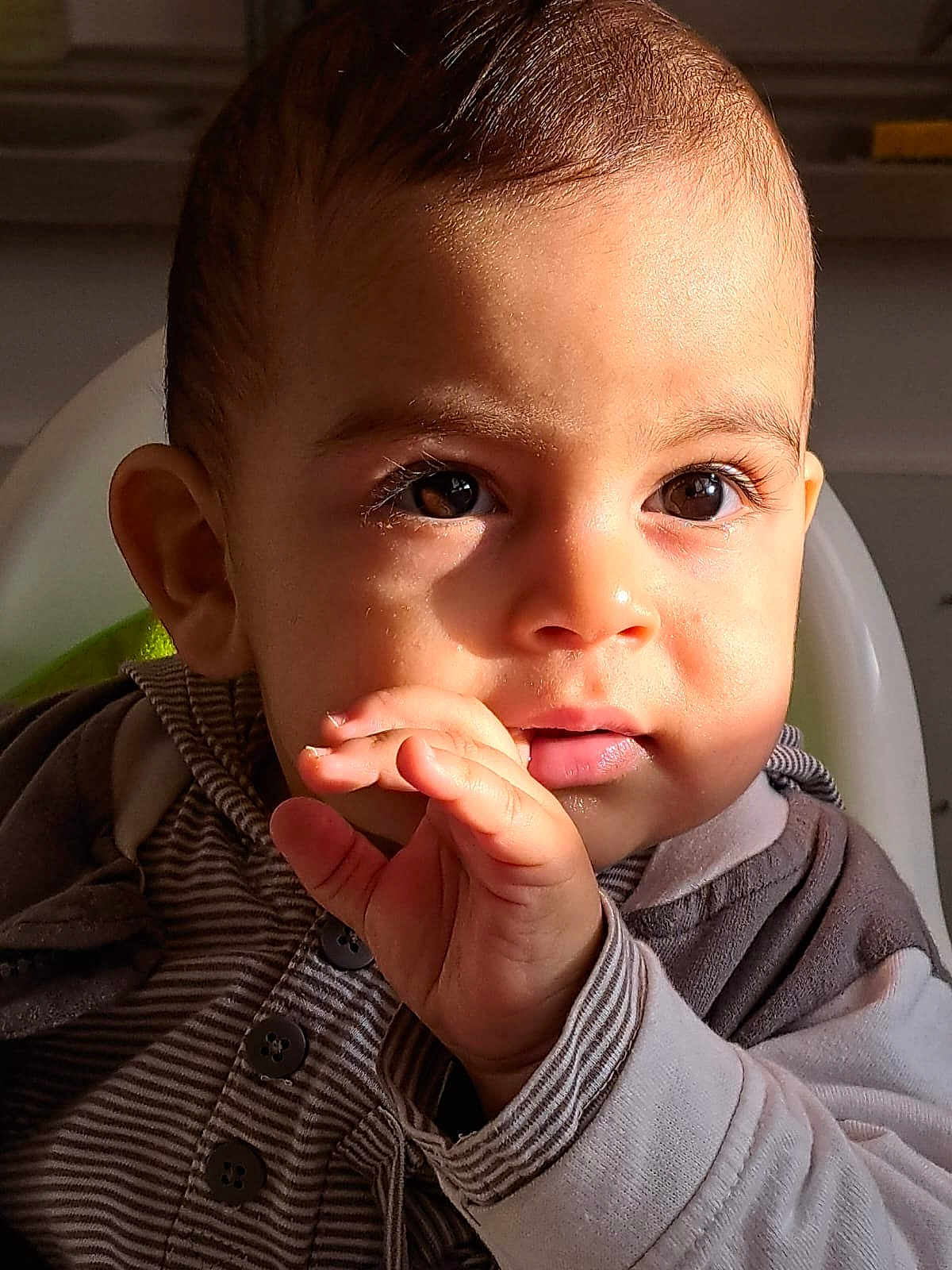 Nahil participe au concours pour gagner de l'argent avec cette photo : baby, child, face, hand, eyes, expression, portrait, closeup, infant, clothing, striped, sitting, cute, indoor, warm_light, skin, young, person, head, fingers