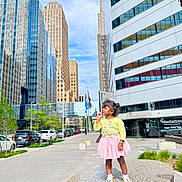 Niva joined the competition — help win amazing prizes! child, girl, urban, cityscape, buildings, skyscraper, sidewalk, pedestal, outdoor, daylight, blue_sky, trees, cars, casual_clothing, playful, smiling, street, modern_architecture, person, young