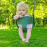 baby, barefoot, casual_clothing, chain, child, curly_hair, daytime, grass, greenery, nature, outdoor, park, playground, portrait, seat, summer, sunlight, swing, toddler, trees