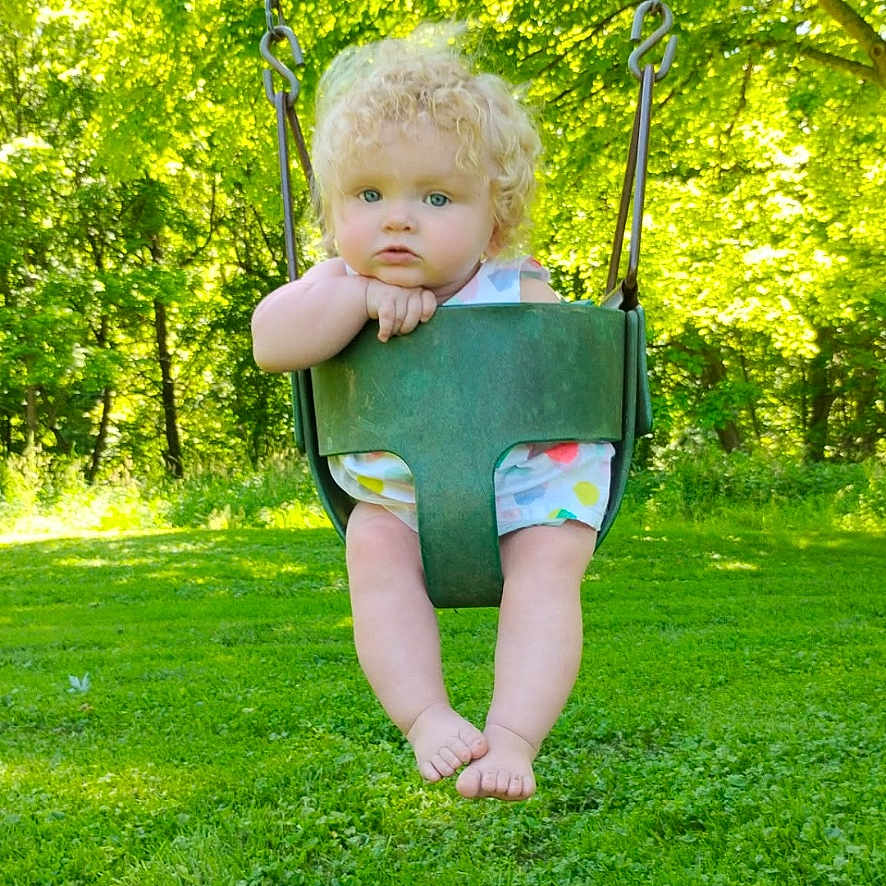 Laikyn joined the competition — help win amazing prizes! baby, barefoot, casual_clothing, chain, child, curly_hair, daytime, grass, greenery, nature, outdoor, park, playground, portrait, seat, summer, sunlight, swing, toddler, trees