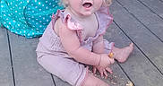 Laikyn is registered to the contest to win money with this photo: baby, backpack, barefoot, blue_eyes, child, crumbs, curly_hair, cute, daylight, expression, innocence, outdoor, person, pink_outfit, polka_dot, portrait, sitting, snack, turquoise, wooden_deck
