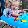 Laikyn is registered to the contest to win money with this photo: air_conditioner, baby, brick_wall, child, concrete, curly_hair, cute, doorway, expression, hair_clips, outdoor, pavement, person, plant, socks, standing, sunflower, toy, walker, window