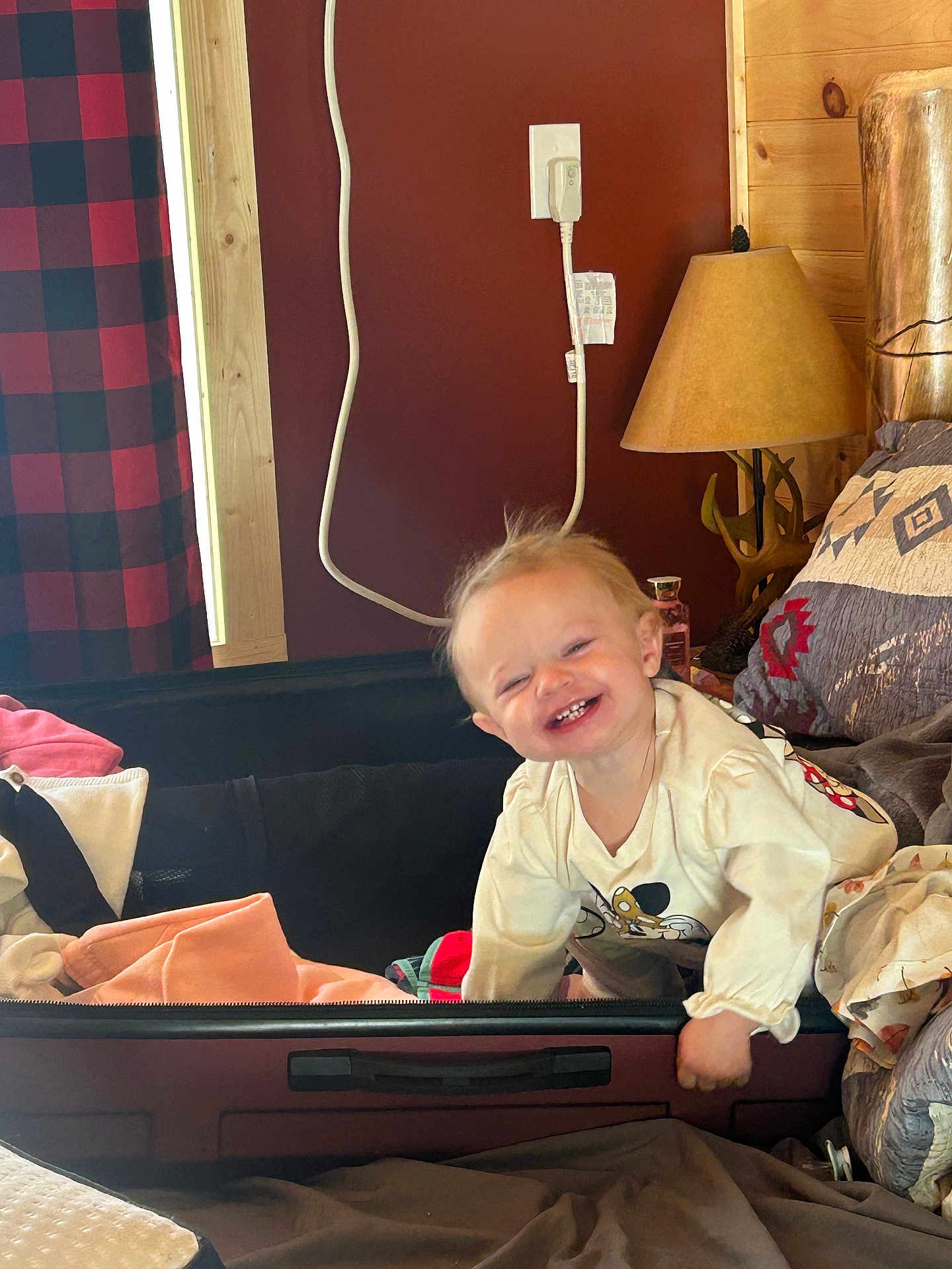 Elianna joined the competition — help win amazing prizes! toddler, child, smiling, suitcase, clothing, indoor, lamp, pillow, blanket, wooden_wall, curtain, happy, face, person, bed, fabric, playful, room, cushion, cord