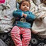 baby, belt_design, blue_top, child, comfortable, cozy, cushion, cute, fabric, face, head, indoor, infant, lying_down, pacifier, patterned_blanket, portrait, soft_toys, striped_pants, young_child