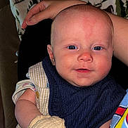 Asher is registered to the contest to win money with this photo: baby, infant, mittens, blue_eyes, bib, blanket, hand, person, clothing, face, smiling, indoor, portrait, cute, skin, head, sitting, comfort, young_child, pattern