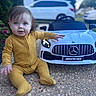 baby, child, yellow_onesie, toy_car, mercedes, amg, outdoor, driveway, pebble, curious, blue_eyes, sitting, small_toy, car, vehicle, garden, plants, daylight, portrait, cute