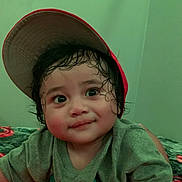 Gm joined the competition — help win amazing prizes! child, toddler, cap, red_cap, wet_hair, curly_hair, smile, lying_down, bedspread, floral_pattern, green_shirt, indoor, face, cute, person, young_child, portrait, expression, casual_clothing, closeup