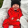 baby, smiling, red_tracksuit, black_beanie, bear_ears, blanket, outdoor, grass, happy, child, infant, clothing, cold_weather, portrait, sitting, cute, cozy, face, person, fashion