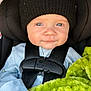baby, child, car_seat, black_hat, blue_clothing, blanket, green_blanket, harness, seatbelt, infant, face, portrait, cute, indoor, child_seat, knit_hat, looking_at_camera, baby_clothes, young_child, close_up