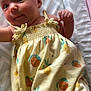 baby, infant, child, yellow_dress, fruit_pattern, chevron_pattern, changing_pad, cute, smiling, lying_down, clothing, fabric, skin, face, hand, head, person, indoors, soft_light, newborn