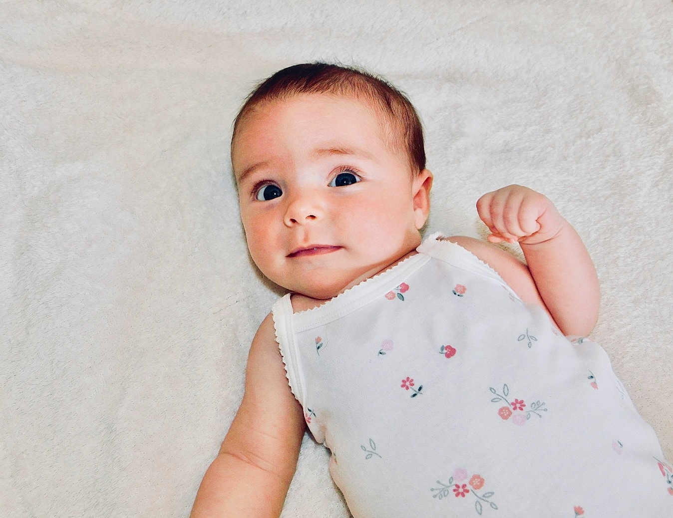 Alora joined the competition — help win amazing prizes! baby, infant, face, eyes, arm, onesie, floral_pattern, blanket, skin, cute, child, lying_down, expression, newborn, person, soft_texture, small_hand, adorable, portrait, indoors