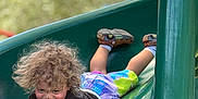 Xyaire is registered to the contest to win money with this photo: active, casual_clothing, child, colorful_clothing, curly_hair, daylight, fun, green_slide, happy, nature_background, outdoor, play, playground, shoes, slide, smile, socks, summer, toddler, young_child